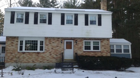 A two-story house with brick and white siding is surrounded by snow.