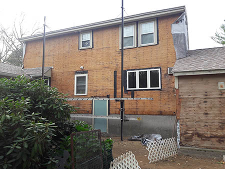 Back view of a house under renovation, stripped to plywood, with scaffolding.