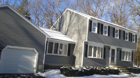 Two-story gray house with white trim and black shutters in a snowy setting.