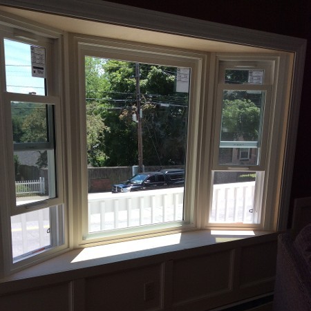 A sunlit bay window with three sections reveals a view of a suburban street.