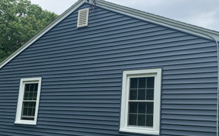 A blue house exterior with two white-framed windows and a triangular roof.