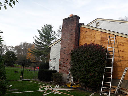 House exterior under renovation, featuring chimney and plywood-covered wall.