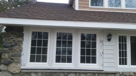 Three white-framed windows with grid patterns set in a stone wall, under a brown shingled roof.