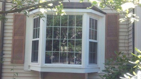 A white bay window with multiple panes on a beige house, framed by brown shutters.