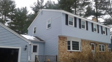 A two-story house with light blue siding, a brick section, and a snow-covered roof.