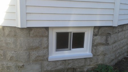 A small basement window with white trim set in a gray stone foundation.
