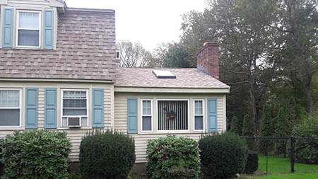 A suburban house with beige siding and light blue shutters, features a sloped roof with a skylight.