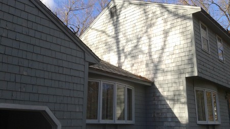 Gray shingled house with large windows on a sunny day.