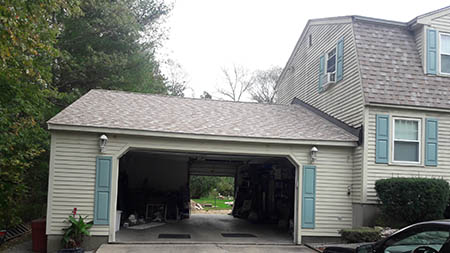 A two-car garage attached to a suburban house with beige siding and grey-blue shutters.