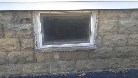 A small, rectangular basement window set in a textured stone wall with visible wear.