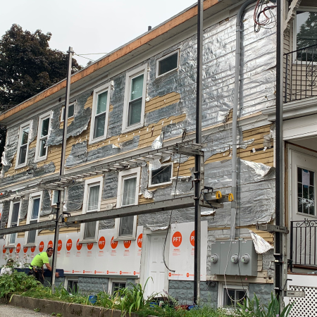 A two-story building with damaged siding and exposed insulation is under repair.