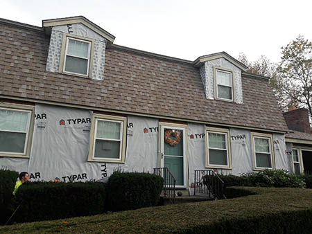 A house under renovation with Typar wrap on the exterior, two dormer windows, and a wreath on the door.