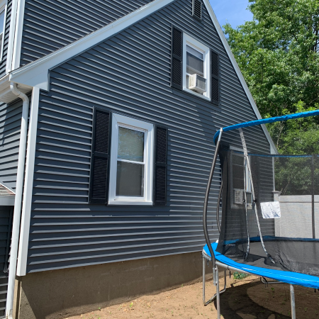 A gray house with black shutters and air conditioning unit is shown beside a large trampoline.