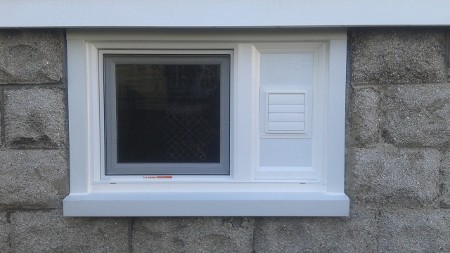 A small, rectangular basement window set in a rough grey stone wall.